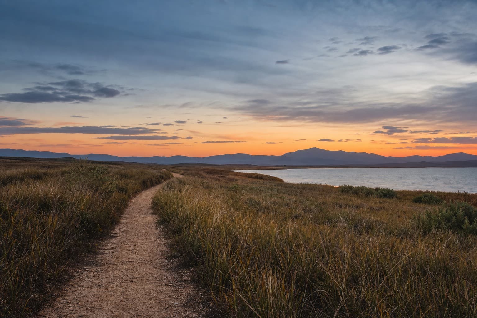 An open lakeside trail toward distant mountains at dusk